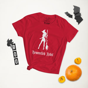 Woman's red t-shirt with image phrase: Broomstick rebel, with image of witch silhouette holding a broom, surrounded by star. Front view. Halloween, spooky season.