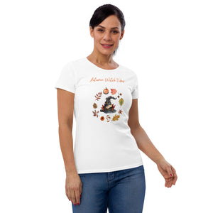 Woman modeling/wearing woman's white t-shirt with image phrase in light orange font: Autumn Witch Vibes, with image of picturebook witch hat adorned with brown vines, autumn leaves, red-orange berries. A circle of leaves, acorns, pinecone, daisy flower, and mushroom, encircled the hat. Front view. Halloween, spooky season.